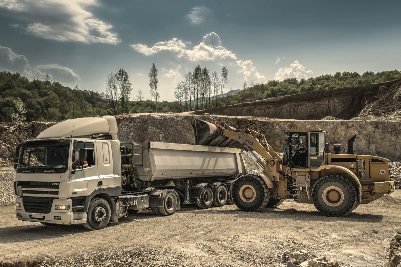 Services Excavator and truck working together in a quarry, showcasing industrial equipment and operations.